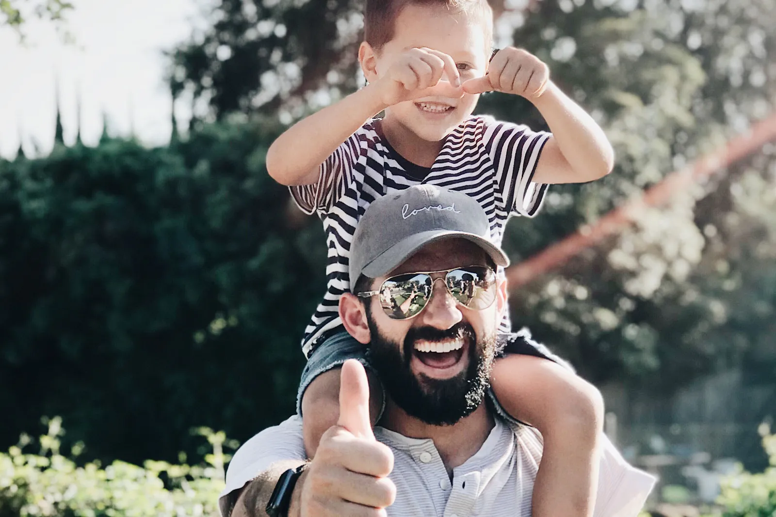 A father giving a thumbs up with his son on his shoulders